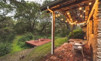 a brick patio with a wooden roof and string lights is surrounded by trees and bushes at William Bay Cottages
