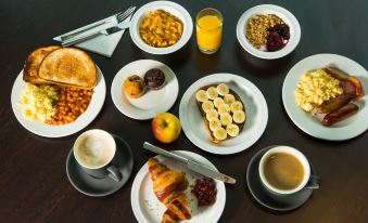 a dining table with a variety of food items , including pastries , fruits , and a cup of coffee at Holiday Inn Express East Midlands Airport