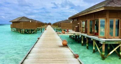 a wooden walkway extending into the ocean , with a row of wooden houses on stilts in the background at Vilamendhoo Island Resort & Spa