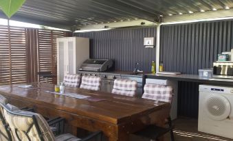 a wooden dining table with chairs and a counter in the background , surrounded by a metal - covered outdoor kitchen at Kadina Village Motel