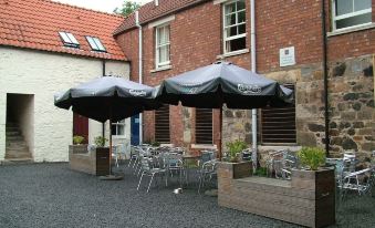 a brick building with an outdoor seating area , featuring several black umbrellas and tables for dining at Aberdour Hotel, Stables Rooms & Beer Garden
