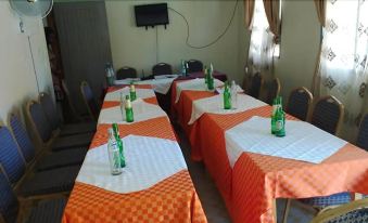 a dining room with multiple tables covered in orange and white tablecloths , each table topped with a bottle of water at Coronation Hotel