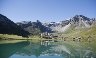 a picturesque mountainous landscape with a calm lake reflecting the sky and buildings , surrounded by snow - capped mountains at Langley Hotel Tignes 2100