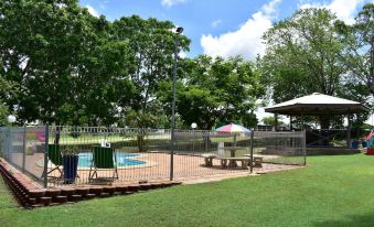 a backyard with a pool surrounded by grass , trees , and a barbecue grill , under a partly cloudy sky at Hillview Motel