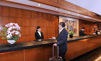 A man stands at the hotel counter with his luggage, while another person is present at The Kimberley Hotel (Tsim Sha Tsui Metropark Hotel)