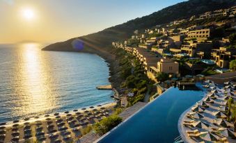 aerial view of a resort with a large pool surrounded by lounge chairs and umbrellas , situated on a hillside overlooking the ocean at Daios Cove Luxury Resort & Villas