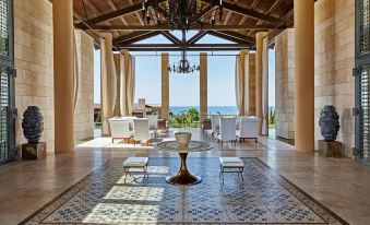 a spacious living room with high ceilings , large windows offering views of the ocean , and white furniture , including tables , chairs , and lamps at The Romanos, a Luxury Collection Resort, Costa Navarino