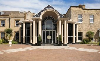 a grand entrance to a building with large columns and a glass door , surrounded by brick walls and a paved walkway at Mercure York Fairfield Manor Hotel