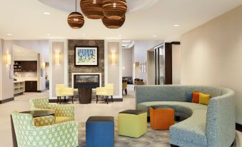 a modern hotel lobby with various seating options , including couches , chairs , and ottomans , as well as a fireplace at Homewood Suites by Hilton Frederick