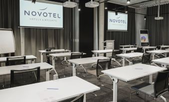 "a conference room with white tables and chairs , a projector screen displaying "" novotel "" in the background" at Novotel Annemasse Centre - Porte de Genève