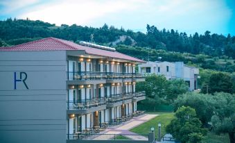 a large building with multiple balconies and a red roof is surrounded by greenery and trees at Royal Hotel and Suites