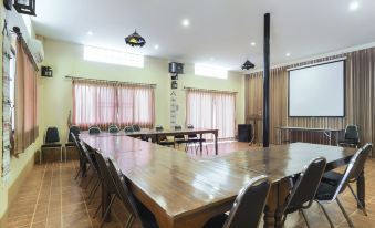 a large conference room with multiple wooden tables and chairs , a projector screen , and a projector screen on the wall at Phufatara Resort
