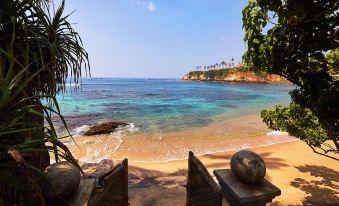 a beautiful beach with crystal - clear water , white sand , and lush green trees , providing a serene view of the surrounding landscape at Eraeliya Villas & Gardens