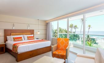 a bedroom with a bed , chair , and table is shown with a view of the ocean through the window at Hotel Dann Cartagena