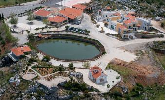 a large building with a round pool is surrounded by smaller buildings and a body of water at Delina Mountain Resort