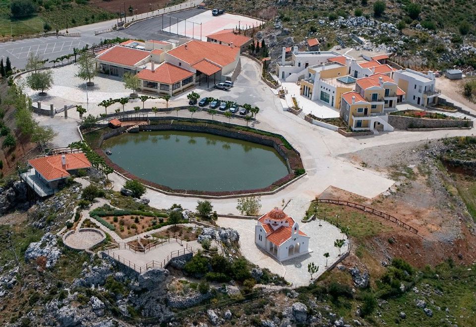 a large building with a round pool is surrounded by smaller buildings and a body of water at Delina Mountain Resort