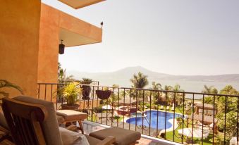 a balcony overlooking a pool and the ocean , with a chair placed on the balcony at El Chante Spa Hotel