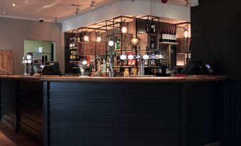 a bar with a black counter and various bottles and cups on display , along with stools and a chandelier at Darlington East (Morton Park)