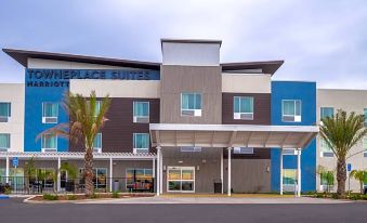 a modern hotel building with a blue and gray exterior , surrounded by palm trees and cars in the street at TownePlace Suites Merced