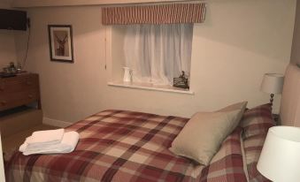 a neatly made bed with a plaid comforter , two pillows , and a window with white curtains at The Black Bull