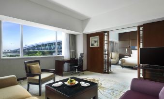 A room with large windows is accompanied by a couch and chair in the adjacent living area at Pullman Guangzhou Baiyun Airport