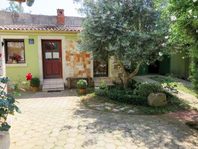 a yellow house with a red door , surrounded by green grass and trees , in a sunny day at Ingrid