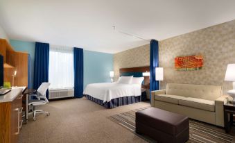 a modern hotel room with a bed , couch , and window , all decorated in neutral colors at Home2 Suites by Hilton Joliet/Plainfield