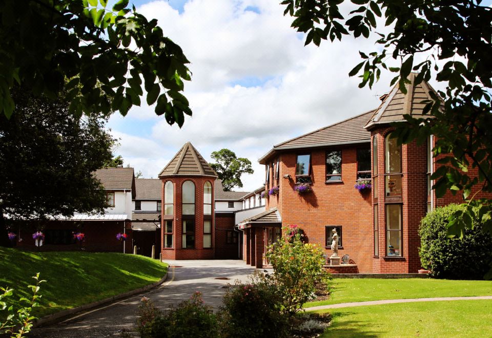 a large brick house with a red roof and white walls is surrounded by trees and bushes at Beaufort Park Hotel