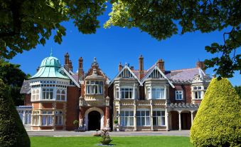 a large red brick house with a green dome , surrounded by a lush green lawn and trees at The Woburn