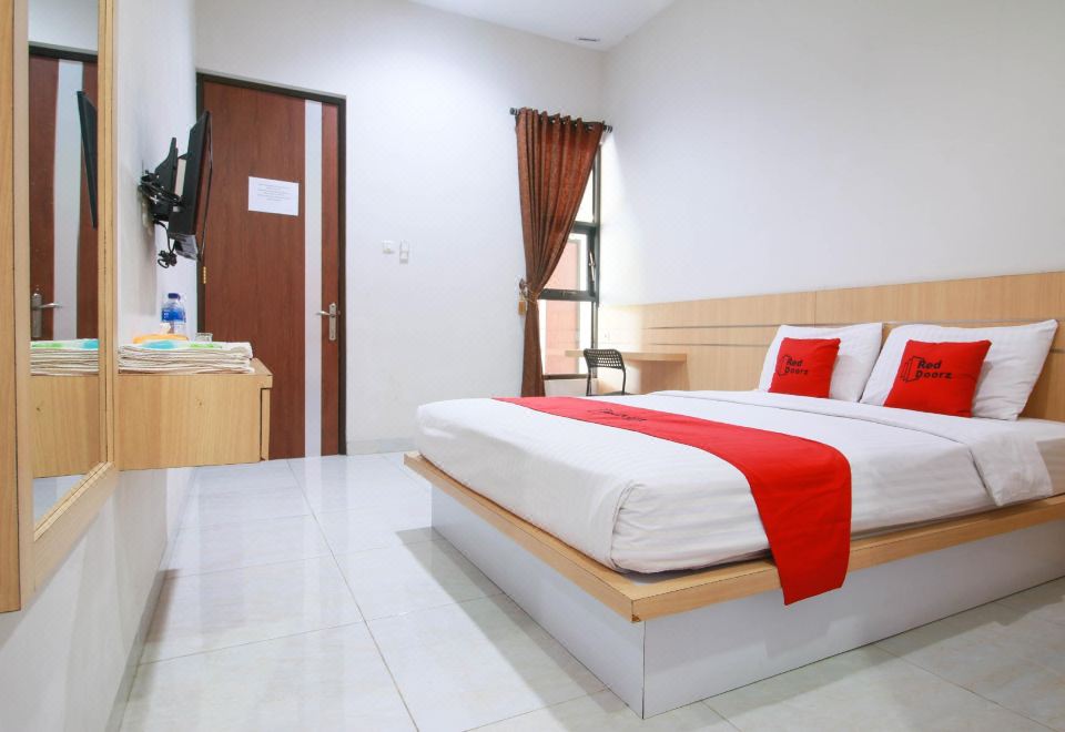 a neatly made bed with a red blanket and white sheets is in a hotel room at RedDoorz Syariah Near Universitas Jenderal Soedirman