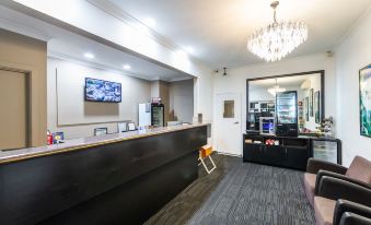 a modern office reception area with a wooden desk , black leather chair , and a television at Golden Age Motor Inn