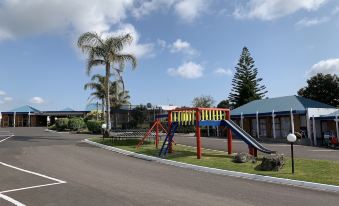 a playground with various play equipment , including swings and slides , located in front of a motel at Cameron Thermal Motel