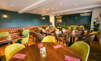 a restaurant with wooden tables and chairs , green walls , and pink napkins on each table at Woodfalls Inn