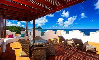 a patio with a view of the ocean and a dining table surrounded by chairs at Cap Maison Resort & Spa