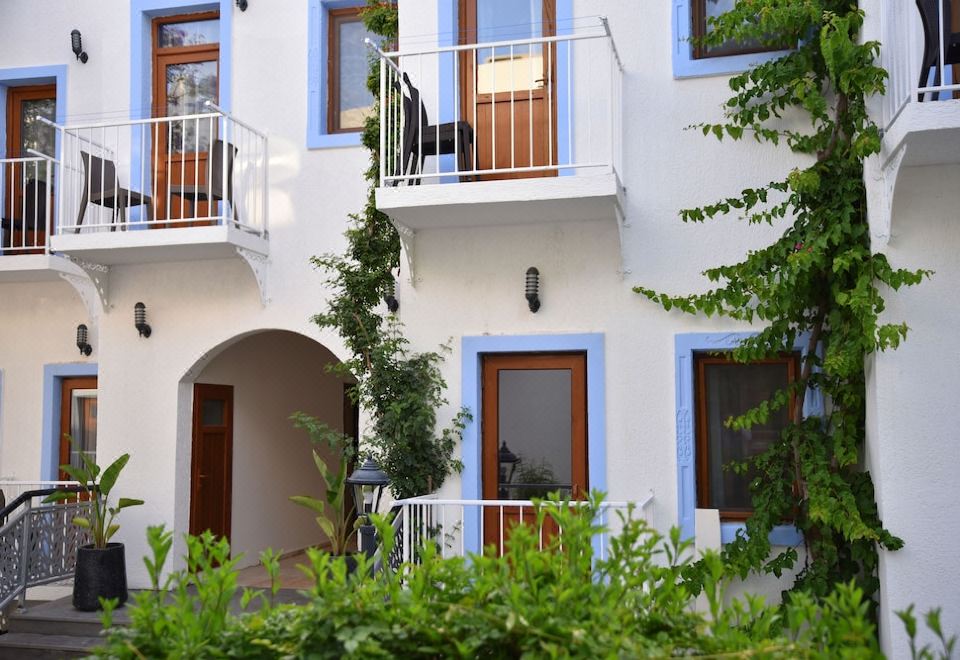 a white building with blue trim , balconies , and windows , surrounded by greenery and trees , giving it a pleasant and inviting atmosphere at Manuela Boutique Hotel Bitez