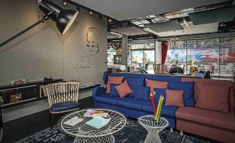 a modern living room with a blue couch , red and orange cushions , and a large lamp at Ibis Styles Geneve Carouge