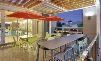 a patio area with multiple tables , chairs , and umbrellas under a wooden roof , providing shade for the dining area at Home2 Suites by Hilton Hagerstown