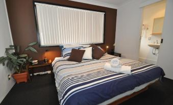 a well - arranged bedroom with a large bed , two lamps , and a window covered by blinds at Beachfront Apartments