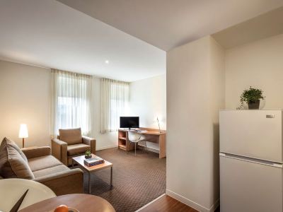 a living room with a couch , chair , and desk in front of a window at Ibis Melbourne Hotel and Apartments