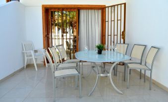 a glass dining table surrounded by white chairs in a room with a sliding glass door at Club Olympus in Garden City