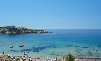 a beautiful beach with umbrellas , sun loungers , and people enjoying the sunny day near the ocean at Panareti Coral Bay Resort