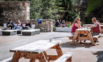 a group of people sitting around wooden picnic tables in an outdoor setting , enjoying each other 's company at The Garret