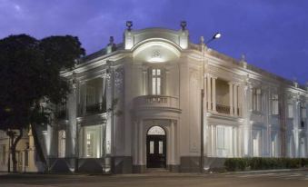 a white , ornate building with columns and a balcony is lit up at night , set against a dark sky at Hotel B