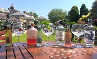 a wooden table with a variety of wine glasses and bottles on it , surrounded by green grass and trees at The Sawley Arms