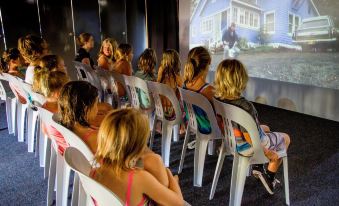a group of children sitting in chairs watching a movie on a projector screen in a room at Discovery Parks - Emerald Beach