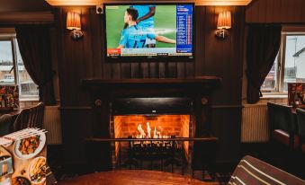 a cozy living room with a large flat - screen tv mounted on the wall above a fireplace , creating a warm and inviting atmosphere at Purple Roomz Preston South