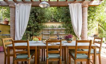 a wooden dining table surrounded by chairs under a covered patio , with a beautiful garden in the background at La Rondine