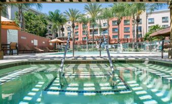 a large swimming pool with a diving board and lounge chairs is surrounded by palm trees and buildings at Courtyard Los Angeles Burbank Airport