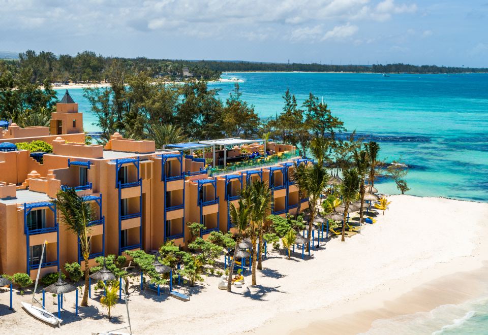 a beachfront hotel with multiple buildings and umbrellas , surrounded by clear blue water and lush greenery at Salt of Palmar, Mauritius