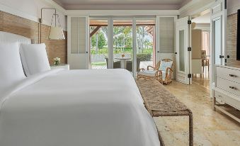 a large , white bed with a tufted headboard is in the middle of a room with two sliding glass doors leading to an outdoor patio at Four Seasons Resort Nevis